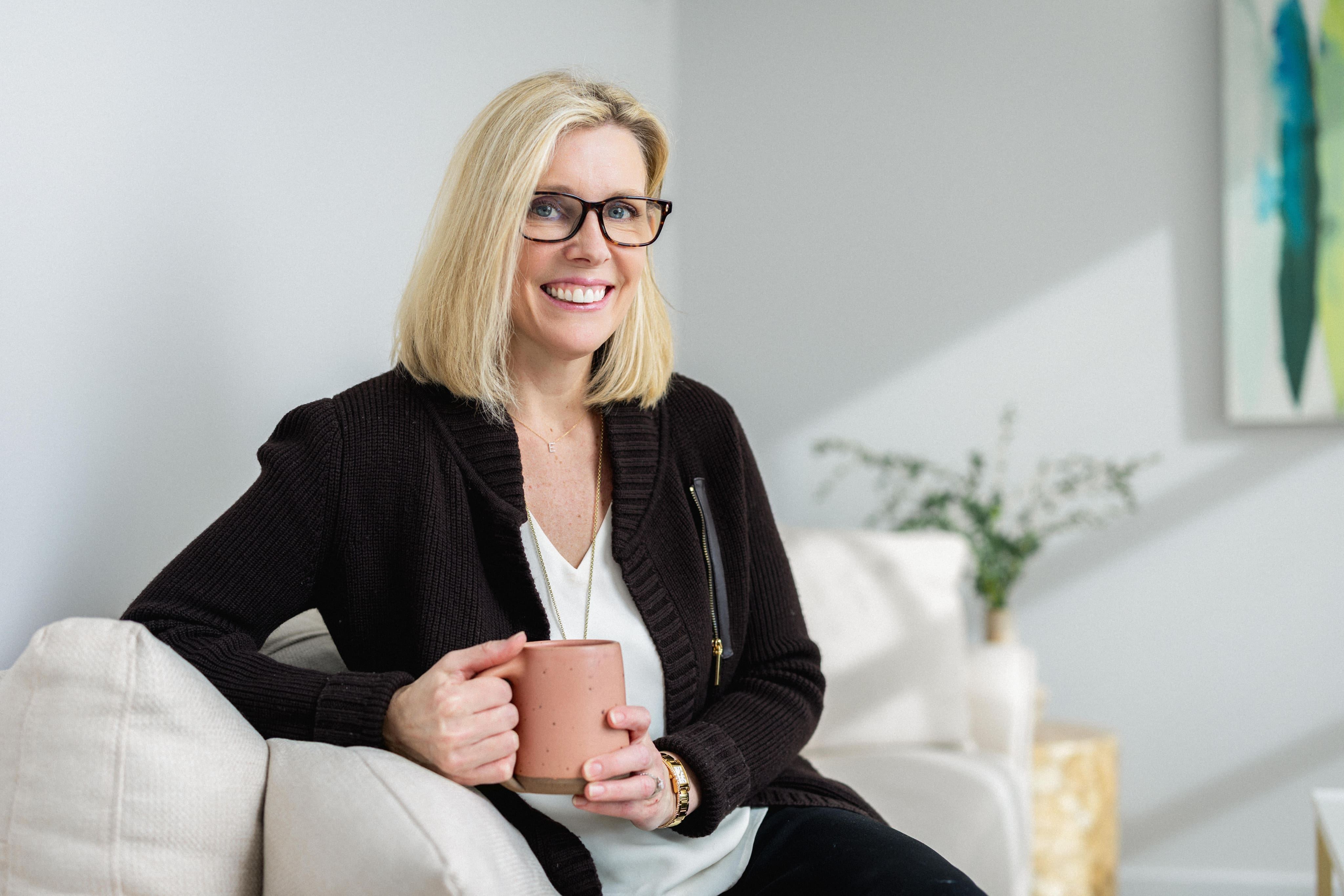 Elisabeth Tullis Schneider, LMFT, seated in an armchair holding a coffee mug and smiling
