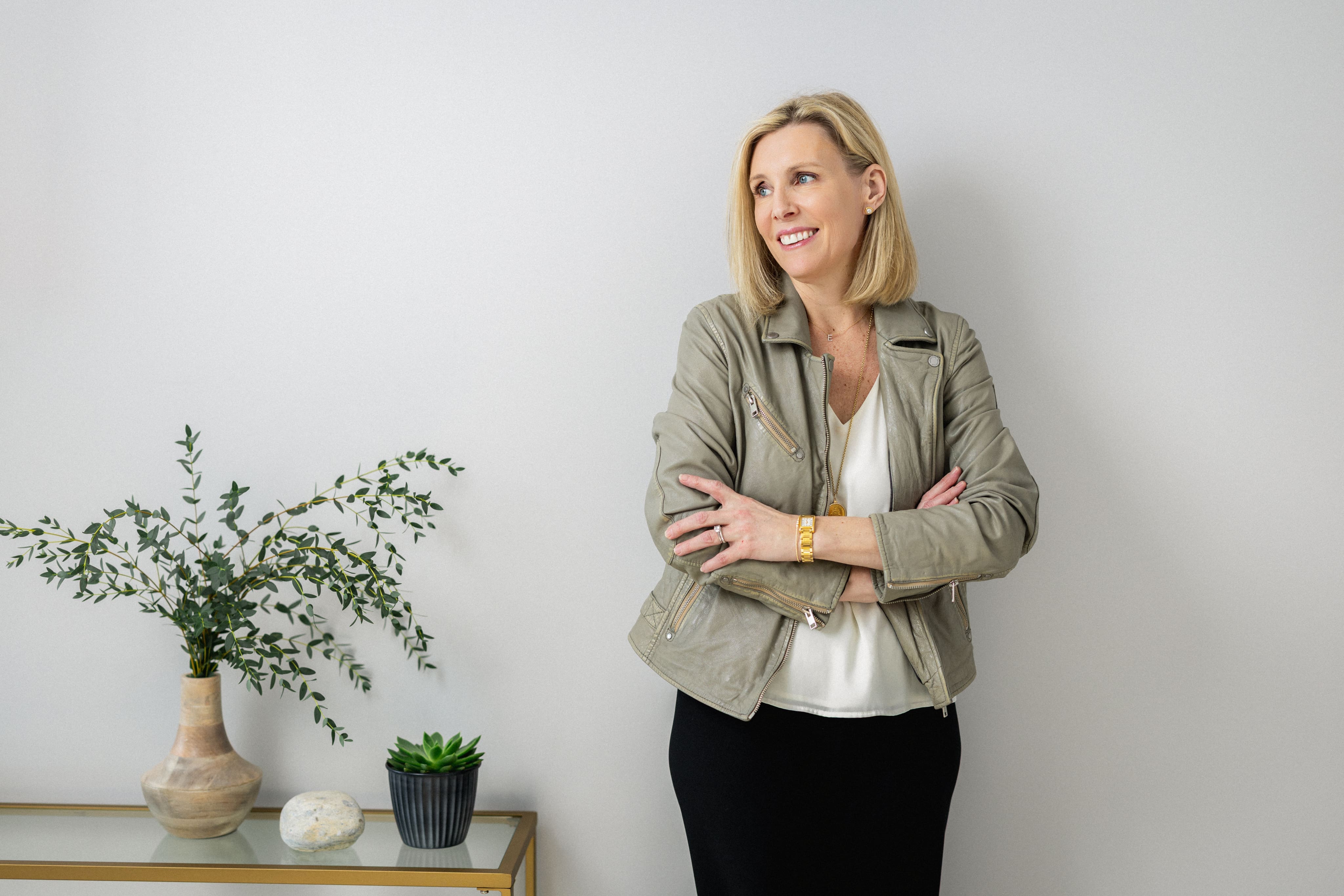 Elisabeth Tullis Schneider, LMFT, standing with arms crossed in a light blazer beside a potted plant
