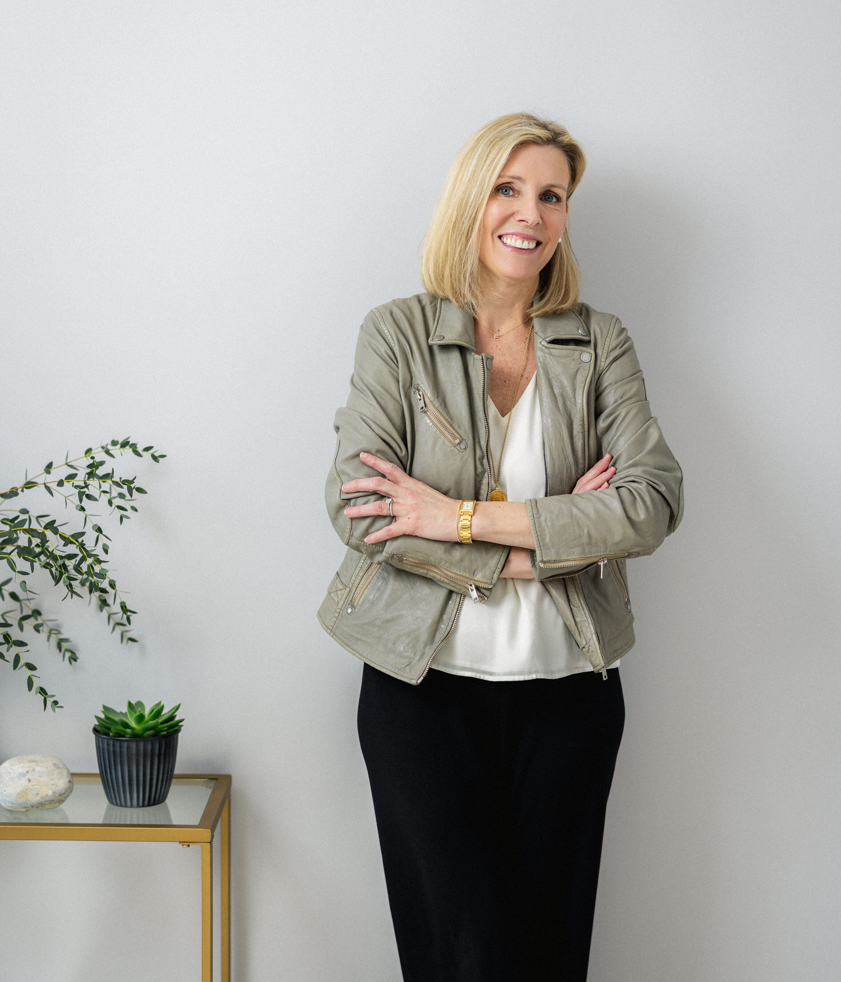 Elisabeth Tullis Schneider, LMFT, standing with arms crossed in a light blazer beside a potted plant