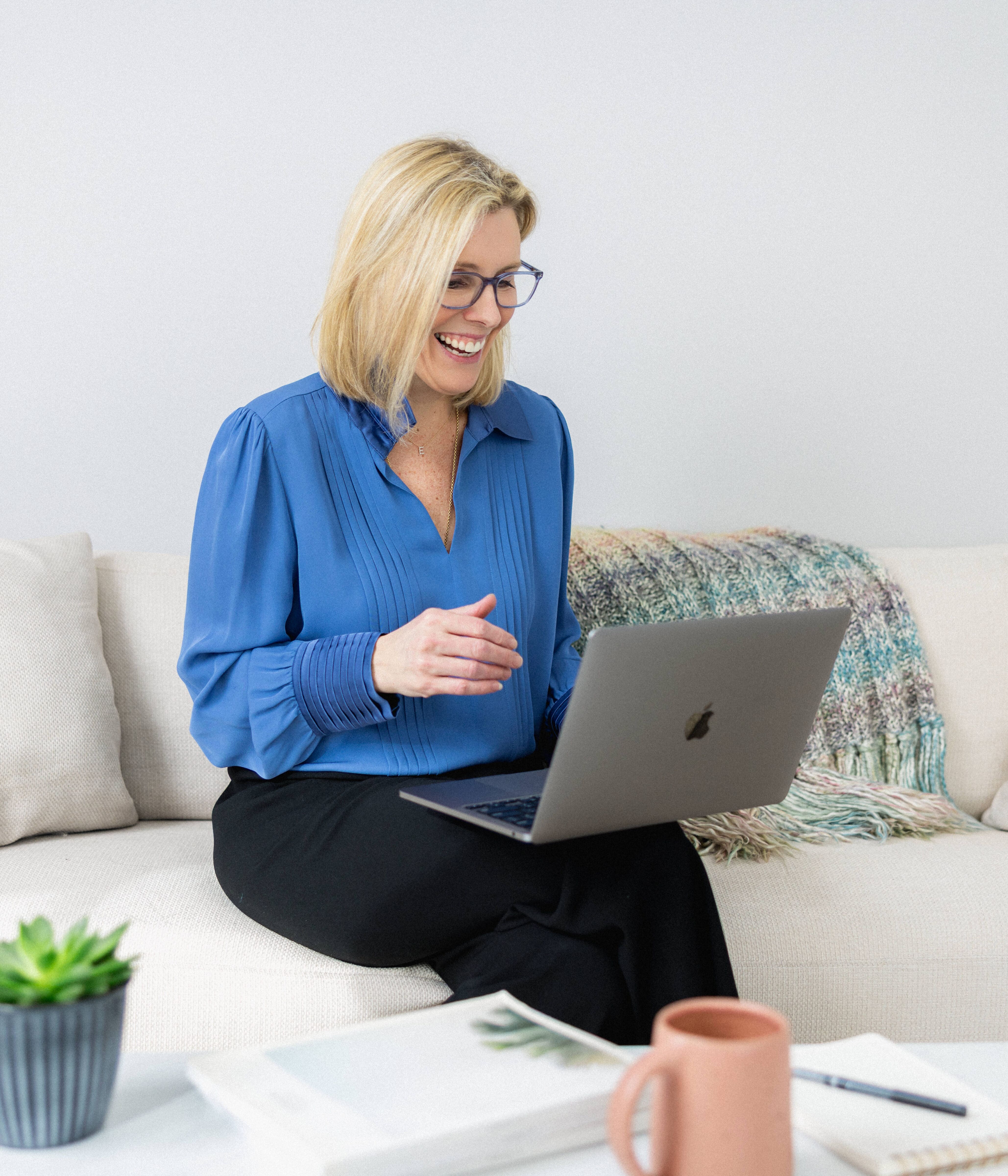 Elisabeth Tullis Schneider looking down at her laptop while seated on a cream sofa