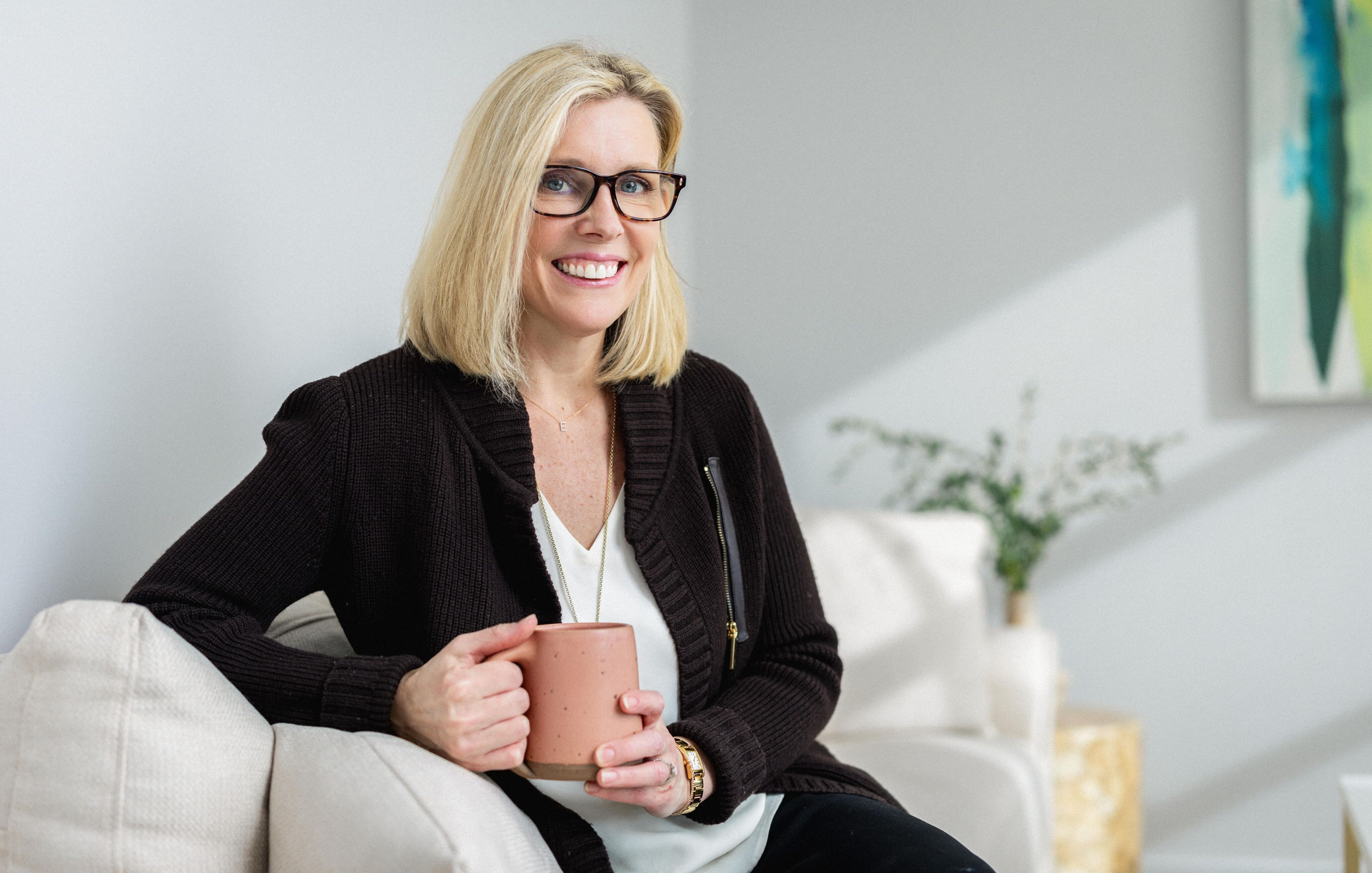 Elisabeth Tullis Schneider, LMFT, seated in an armchair holding a coffee mug and smiling