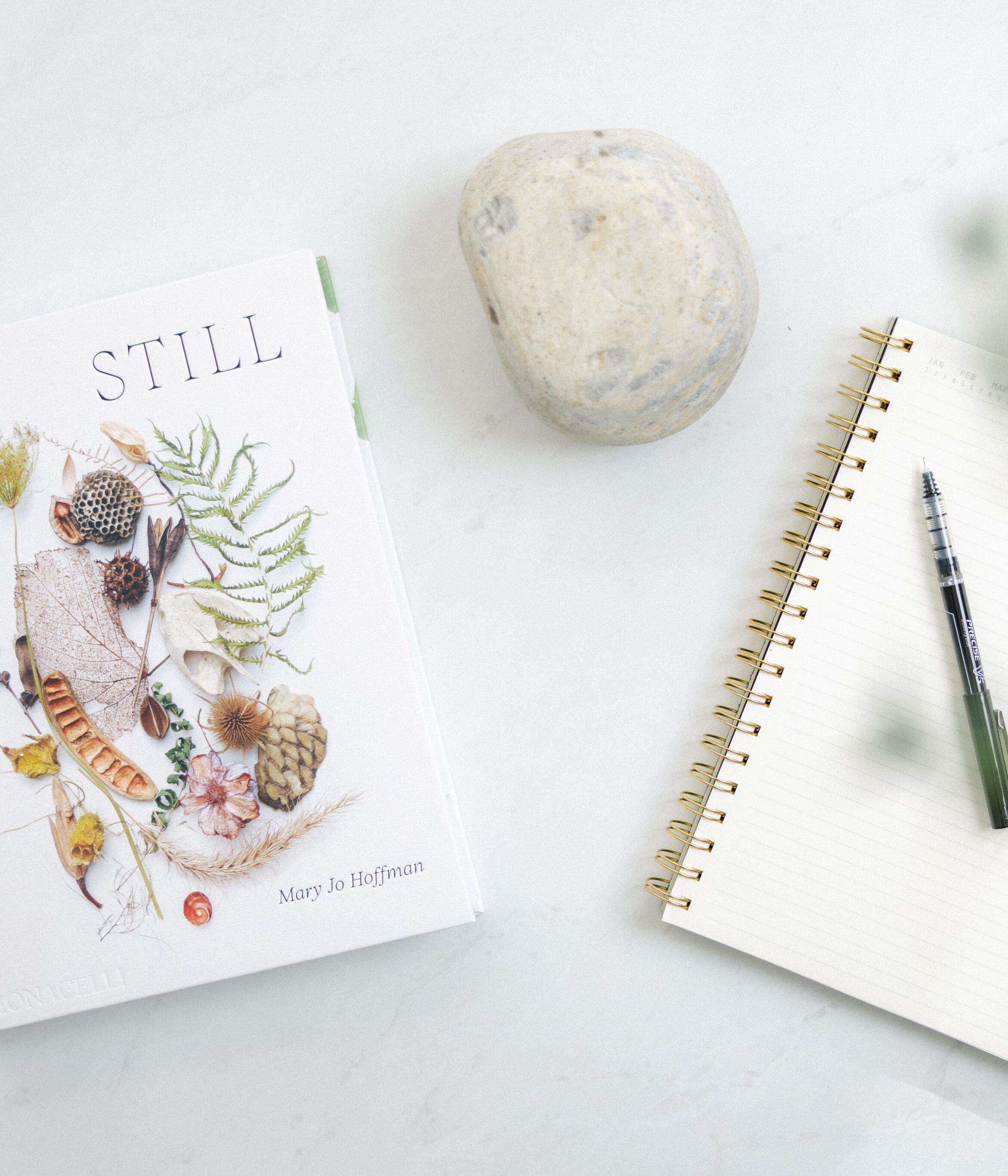 Flat lay of a spiral notebook, pen, smooth stone and yellow flowers on a white desk